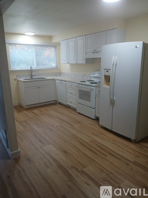 A kitchen with white appliances and wooden floors.
