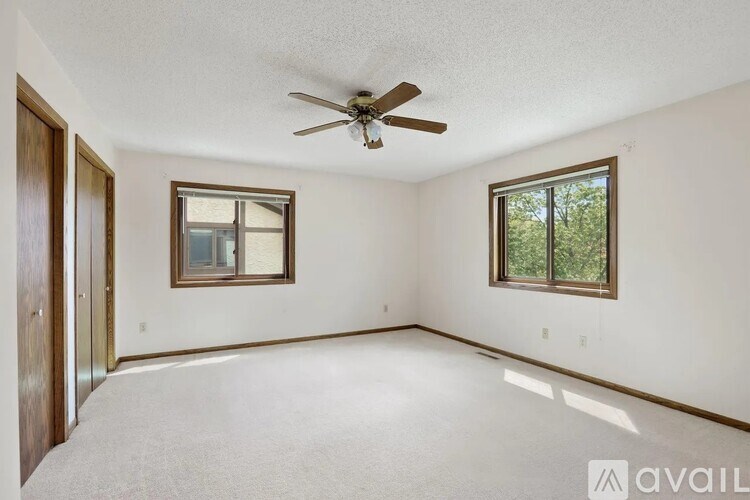 A room with a ceiling fan and two windows.