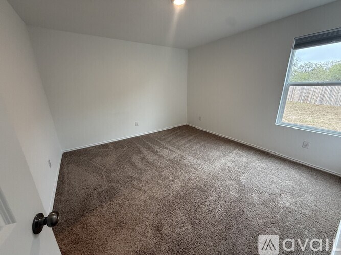A room with brown carpet and a window overlooking a fence.
