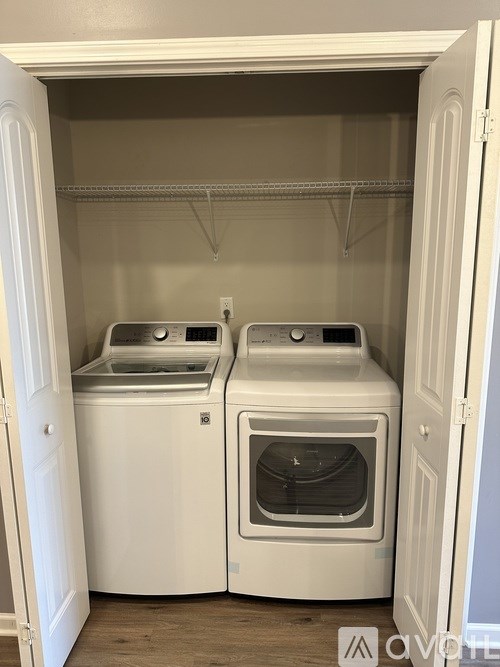 A white laundry machine is in a small, white-walled laundry room.
