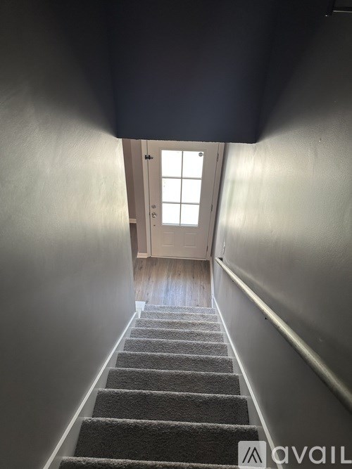 A stairway with a carpeted runner and a wooden handrail leading to a door with a window above it.