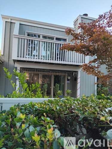 A white building with a balcony and a tree in front.