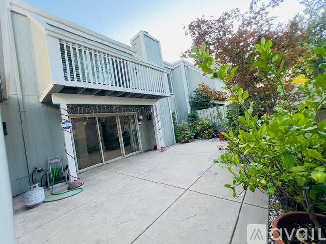 A patio area with a white wall and a tree in the foreground.