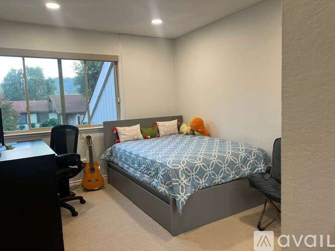A bedroom with a bed, chair, and guitar.