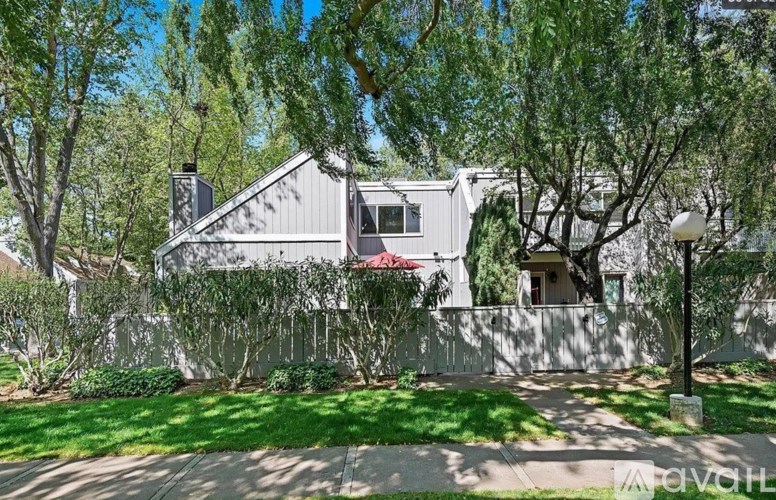 A house with a grey roof and a red awning is surrounded by trees.