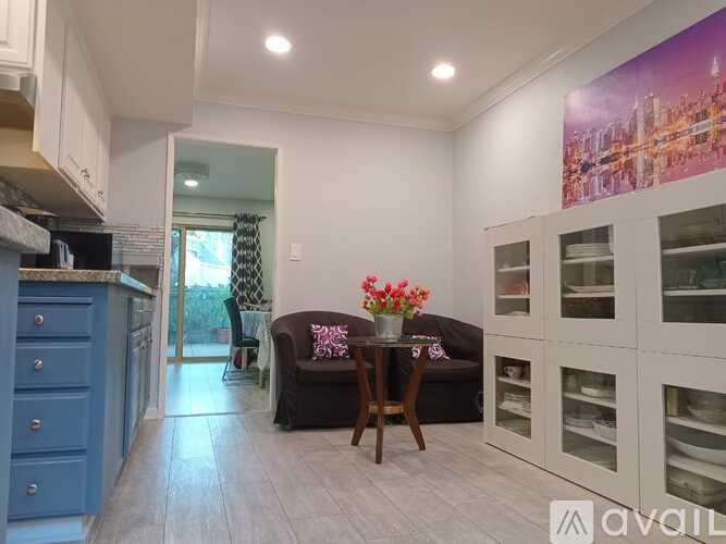 A dining area with a table set for two and a couch with a pillow and a vase of flowers.