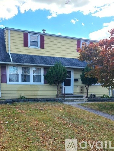 A yellow house with a red window and a tree with orange leaves.
