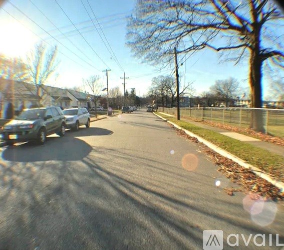 A street with cars parked on the side and trees lining the road.