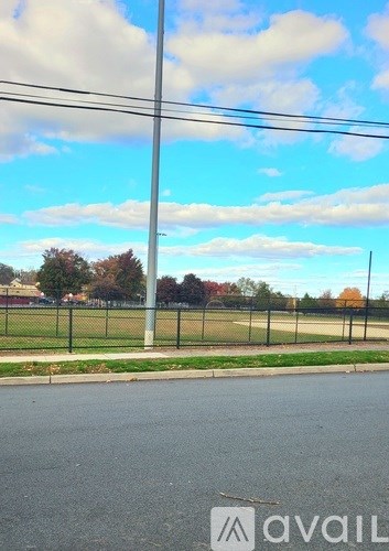 A street view with a fence and trees in the distance.
