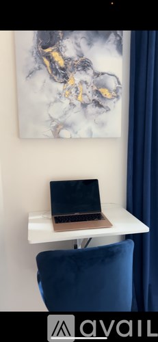 A laptop is on a white desk with a blue chair.