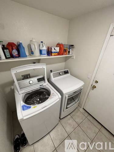 A small laundry room with two washers and a shelf with cleaning supplies.