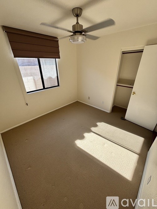 A room with a carpeted floor, a ceiling fan, and a window with blinds.