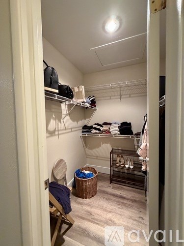 A small closet with clothes on shelves and a chair with a bag on it.