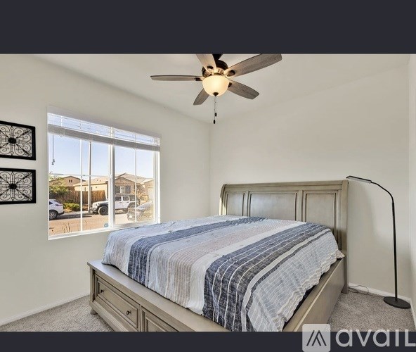 A bedroom with a bed, a ceiling fan, and a window showing a view of houses.