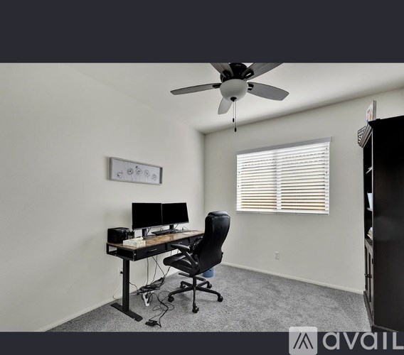 A room with a desk, chair, and a ceiling fan.