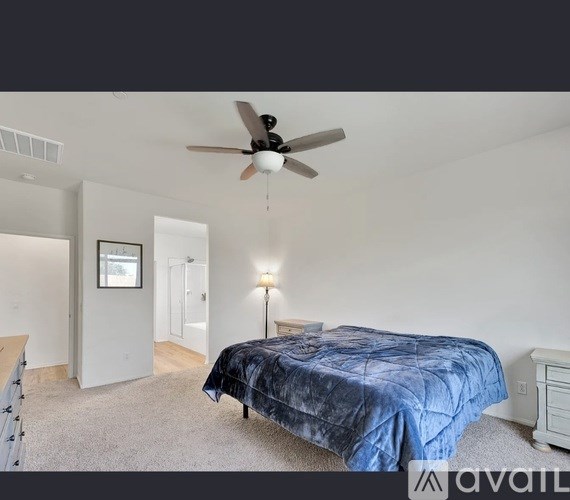 A bedroom with a bed covered in a blue bedspread, a ceiling fan, and a lamp on the side table.