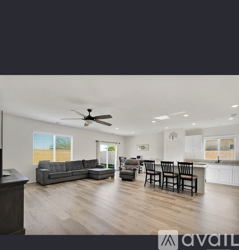 A spacious living room with a grey sofa set and a kitchen area with white cabinets.