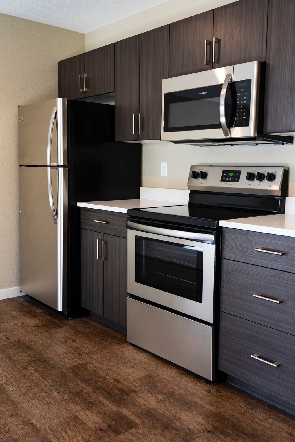 A black fridge and microwave in a kitchen with wooden floors.