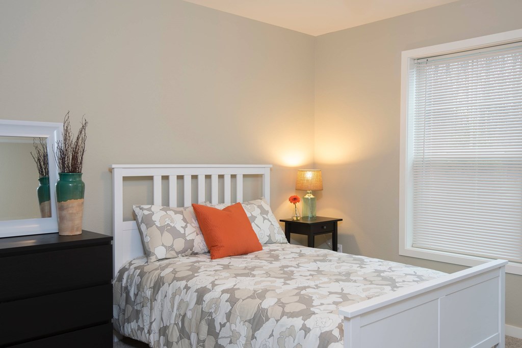 A bedroom with a white bed and a small table with a lamp on it.