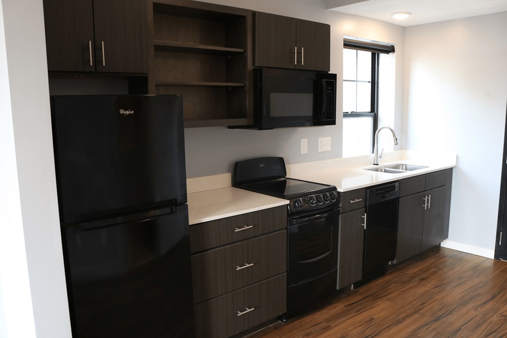 A black fridge and oven in a kitchen with wooden floors.