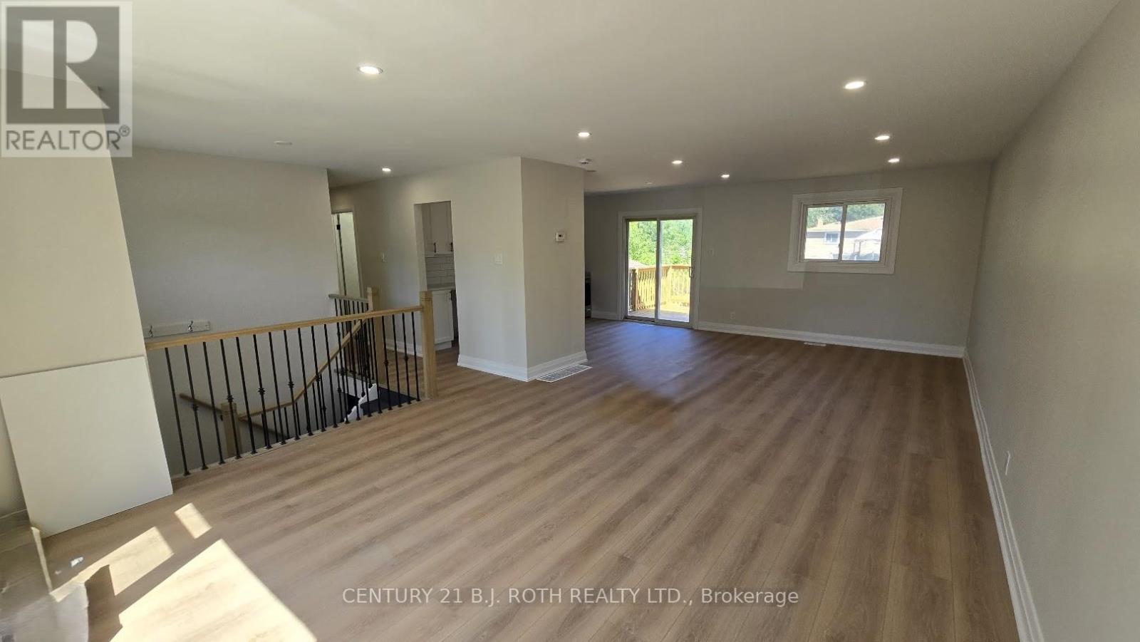 A spacious room with wooden flooring and white walls, with a window on the right side.