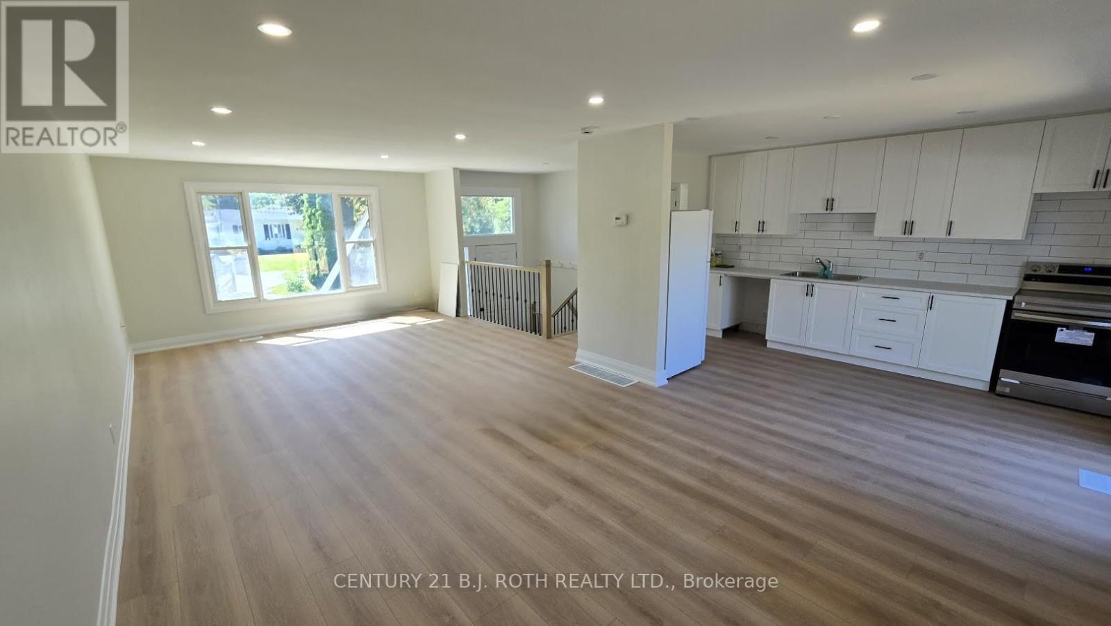 A spacious kitchen and living room with white cabinetry and a hardwood floor.