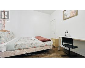 A bedroom with a floral bedspread, a desk with a chair, and a painting on the wall.