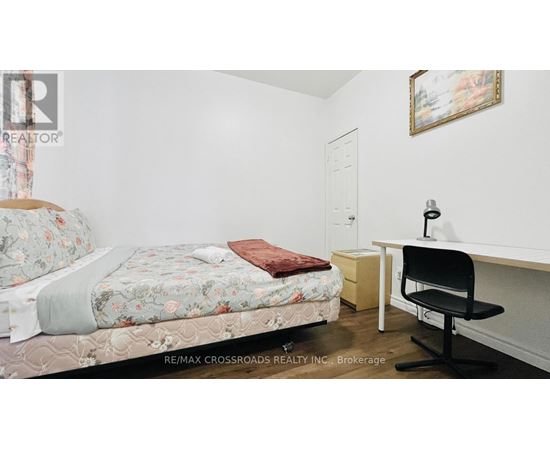 A bedroom with a floral bedspread, a desk with a chair, and a painting on the wall.