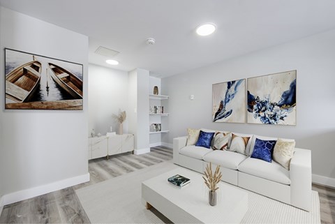A living room with a white couch and a painting on the wall.