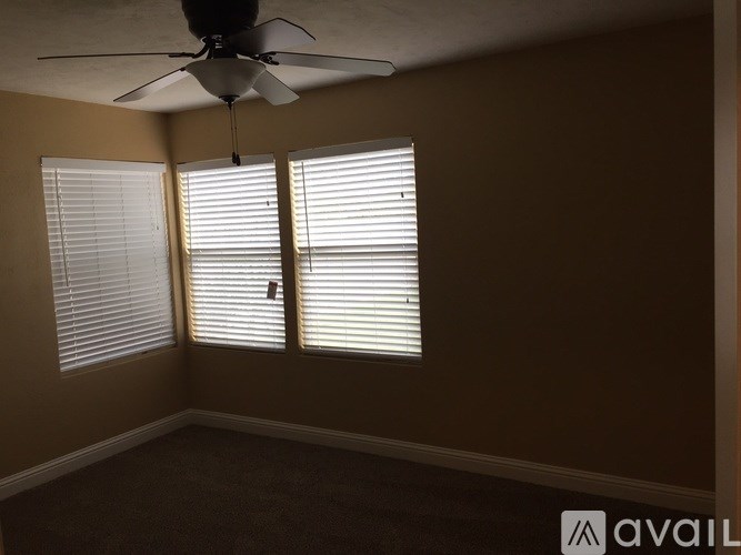 A room with a ceiling fan and two windows with blinds.