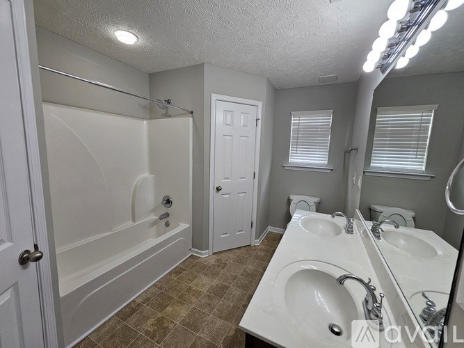 A bathroom with a white tub and sink, brown tiles, and a white door.