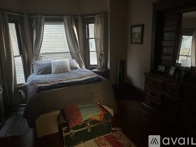 A bedroom with a bed, dresser, and window with curtains.