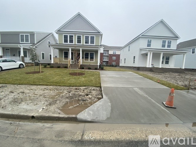 A white car is parked in front of a grey house.