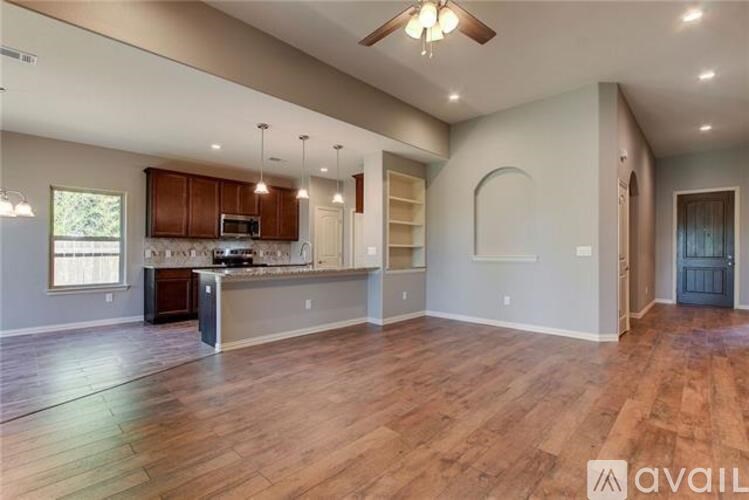 A spacious living room with hardwood floors and a kitchen area in the background.