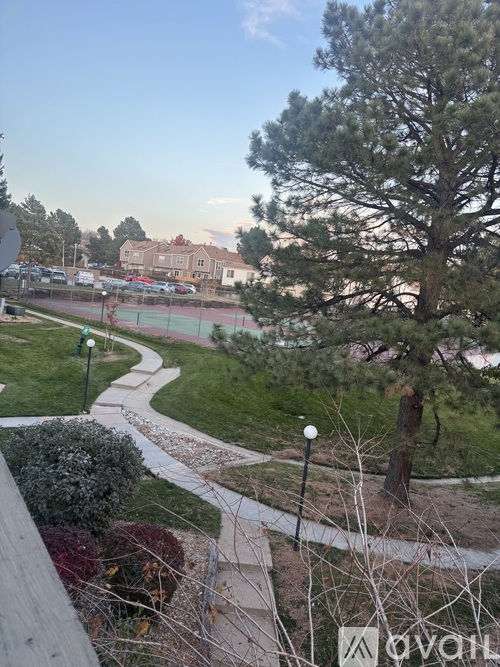 A park with a walking path, a tennis court, and a large tree.