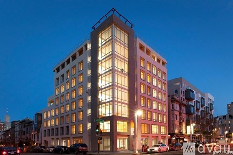 A modern building with a glass facade is illuminated from within, creating a warm glow.