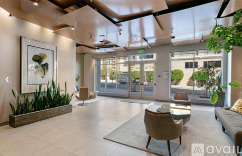 A modern living room with a large painting on the wall and a view of the outdoors through the glass doors.
