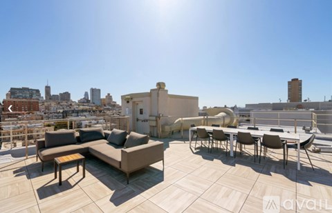 A sunny day on a rooftop patio with a couch, chairs, and a table.