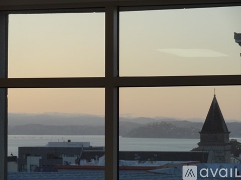 A view of a sunset through a window with a building and a tower visible in the distance.