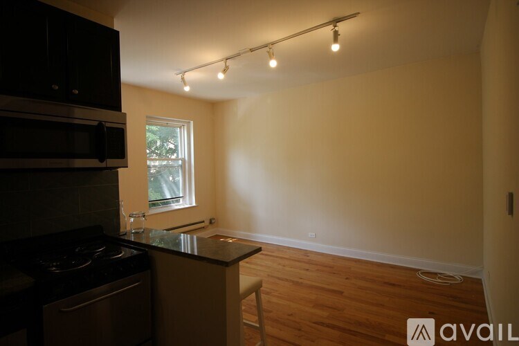 A kitchen with a black stove top oven and microwave, a black counter top, and a window with a view of trees outside.