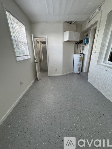 A room with a white floor and walls, a window with blinds, a door, and a white refrigerator.