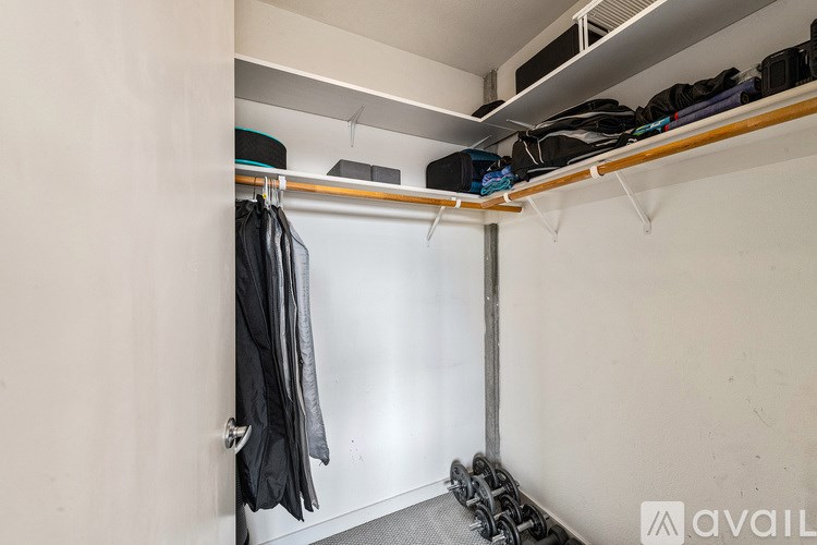 A small, white closet with a black jacket hanging on a rod.