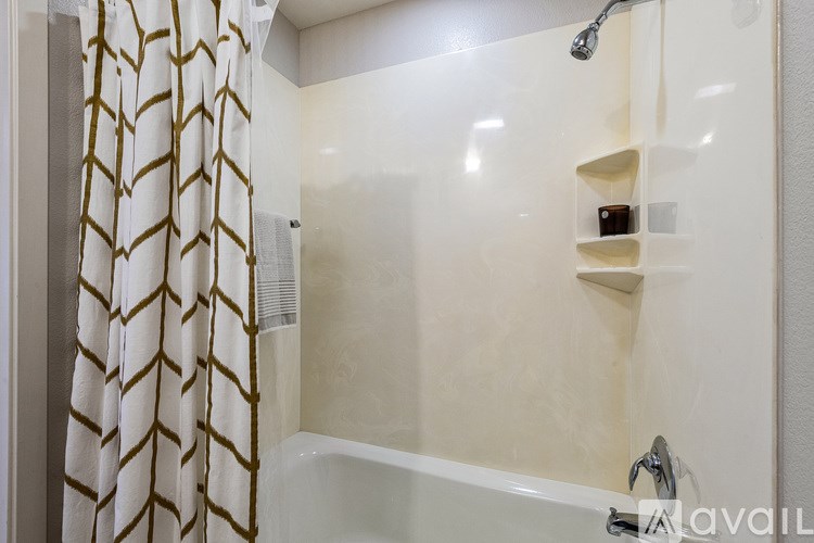 A shower area with a white tub and a gold and white shower curtain.