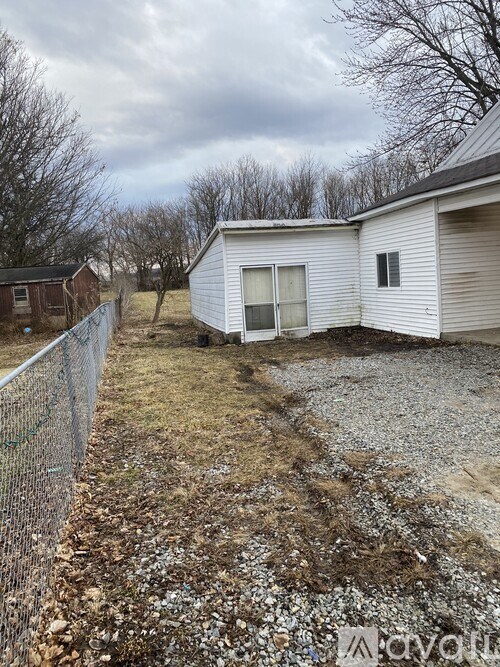 A white mobile home sits in a gravel lot with a chain link fence.