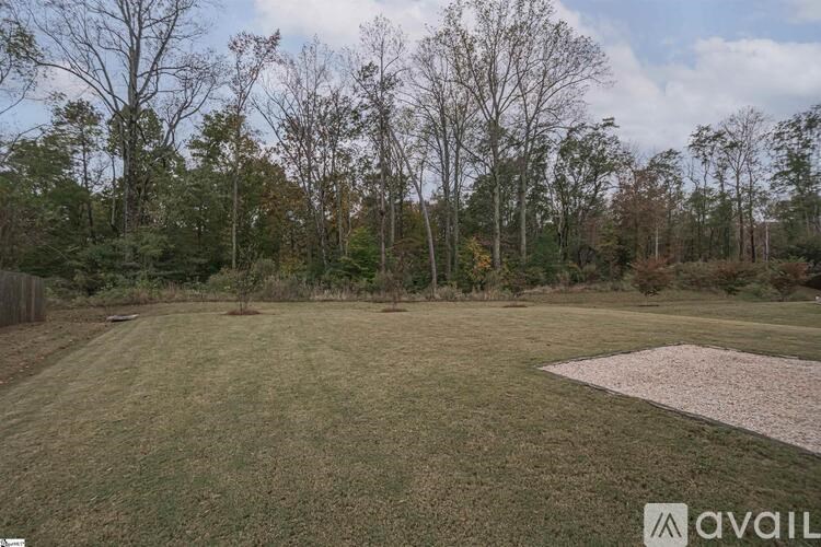 A grassy field with a gravel area and trees in the background.