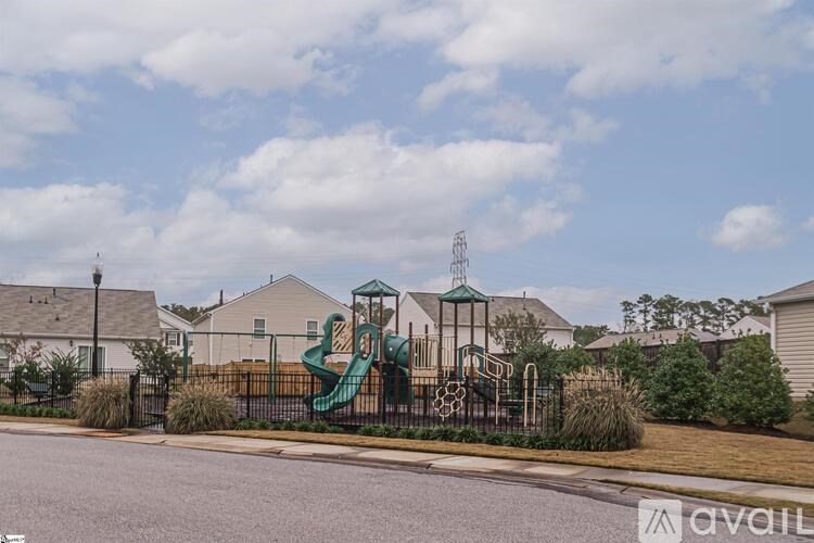 A playground with a green slide and a fence in front of a house.