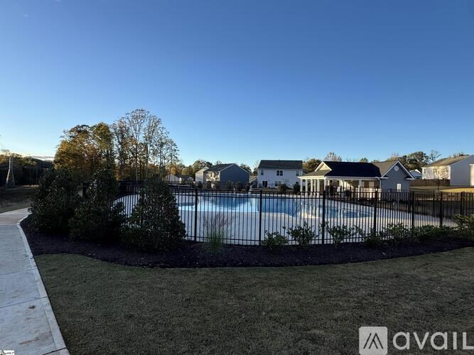 A pool surrounded by a black fence and a grassy area with a house in the background.