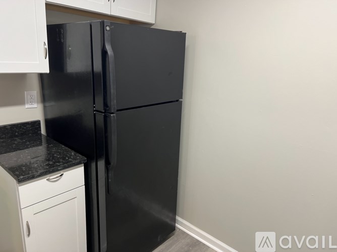 A black refrigerator in a kitchen with white cabinets.