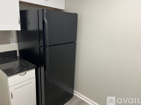 A black refrigerator in a kitchen with white cabinets.