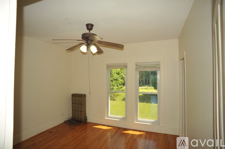 A room with a ceiling fan and a window overlooking a green lawn.